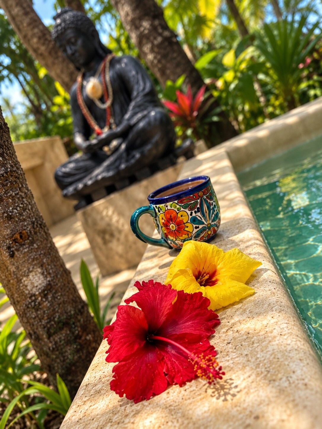 Flowers and a painted cup beside a pool with a Buddha statue