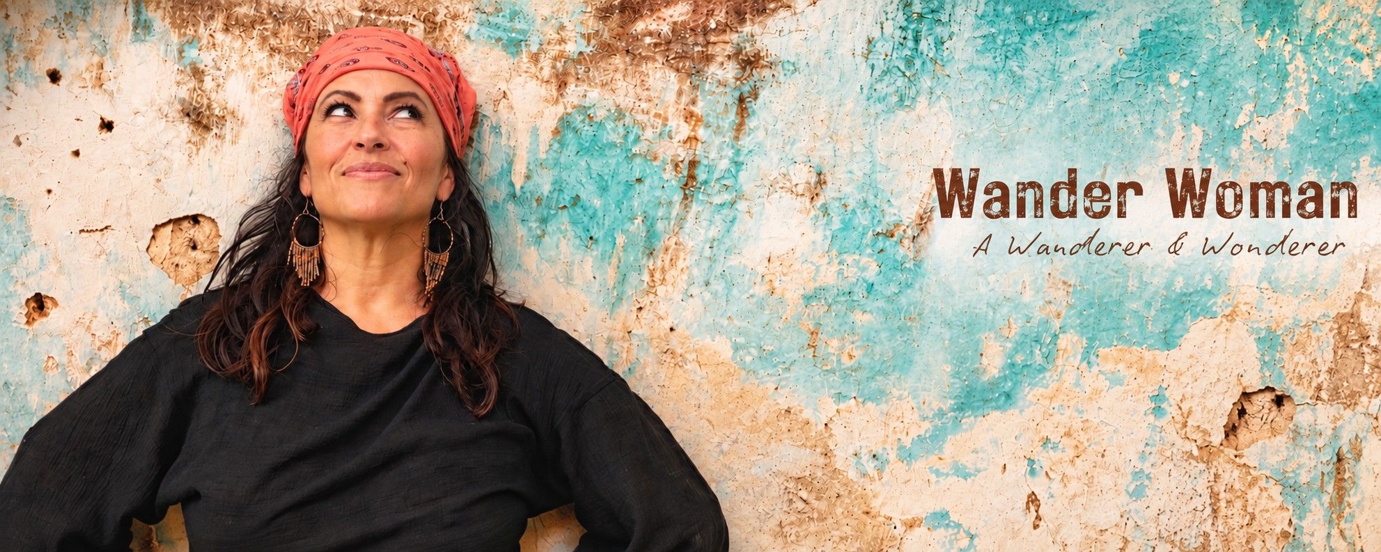 Lori Bellman in a coral head wrap against a turquoise and cream painted plaster wall beside the baked-in text Wander Woman, A Wanderer & Wonderer